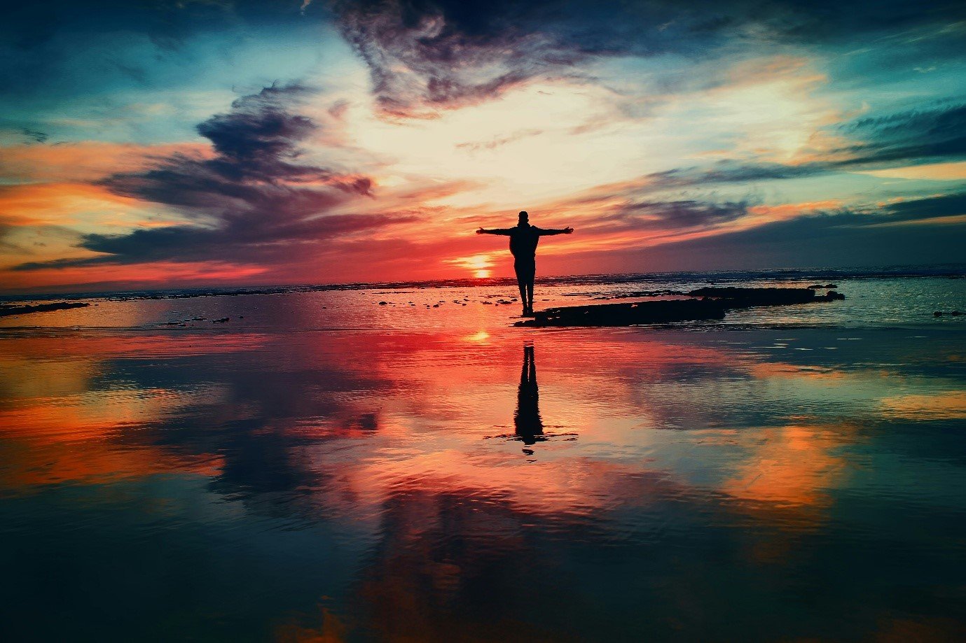 Standing at the beach at sunset with spread arms